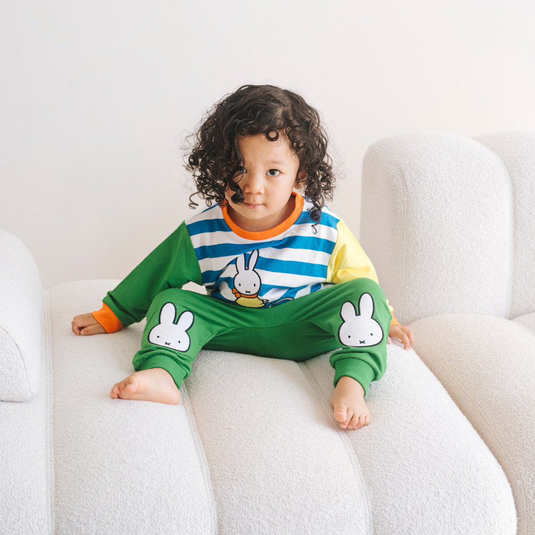 Kind, das das Bambus-Lounge-Set „Move“ in der Farbe Miffy mit einem Sweatshirt mit Fahrradmotiv und einer grünen Jogginghose trägt